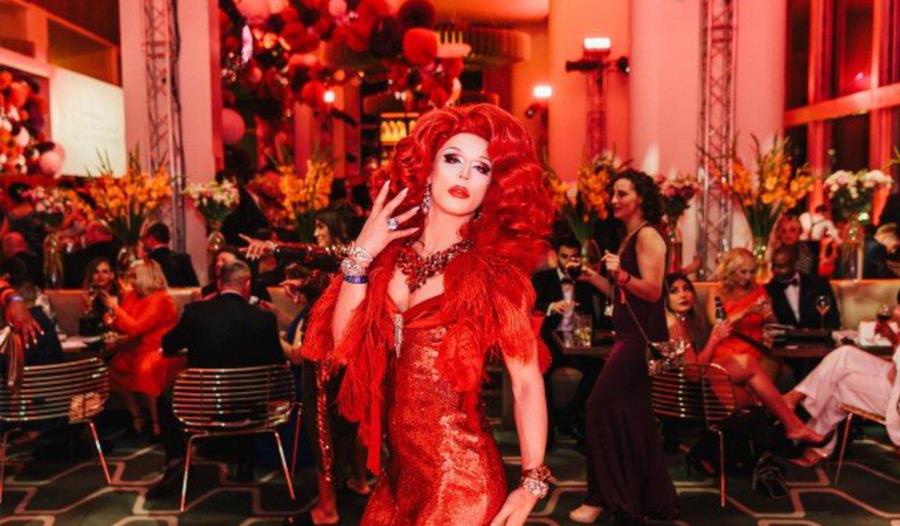 a drag queen in a red dress stood in a function room