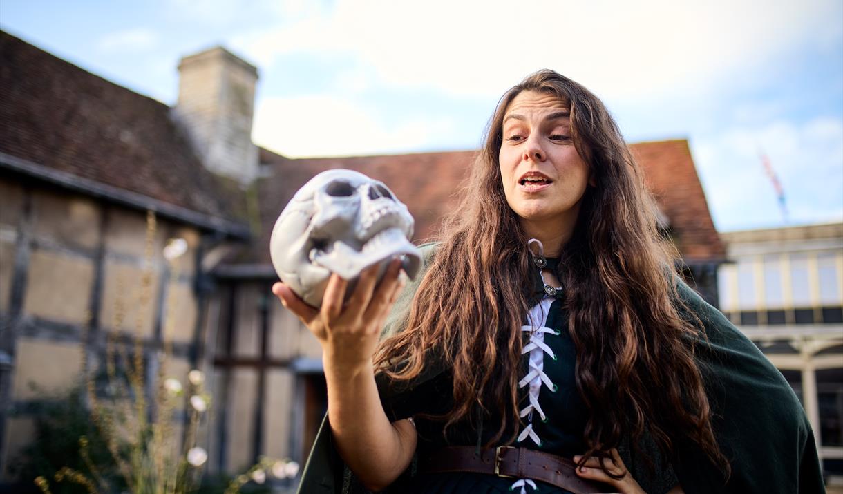 A woman in costume outside Shakespeare's Birthplace reciting to a skull held aloft in her hand