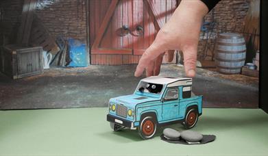 A hand working on a stop start animation of a toy car