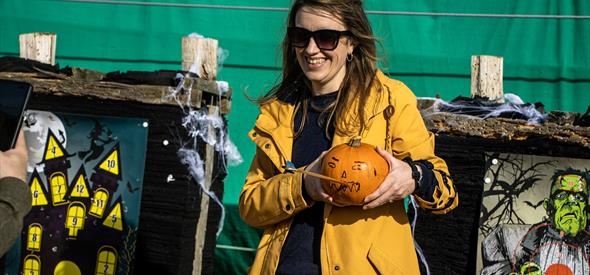 Lady holding a pumpkin in a yellow coat smiling at the camera 