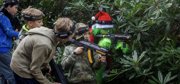 Grinch in a Christmas hat with a paintball gun hiding in the trees with four boys 