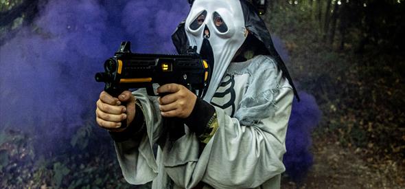 A person in a scream mash with a gun and purple smoke behind them 