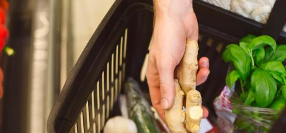 A supermarket basket with fresh produce and a hand holding a bulb of ginger