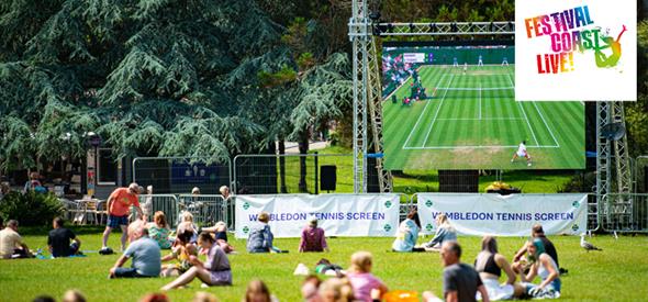 Large screen in the gardens with people sitting on the grass