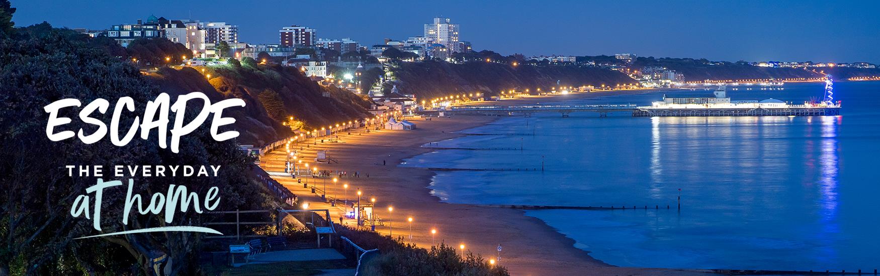 Bournemouth Bay lit up at night with the text Escape the Everyday at home