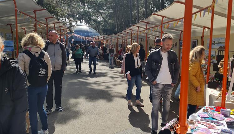 Long shot of market from the entrance with the aviary in the distance, stalls on both sides and people browsing.