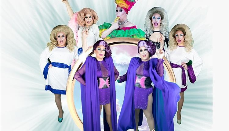 Group of 7 posed drag artistes around a gold ring.  Principle colours purple and white