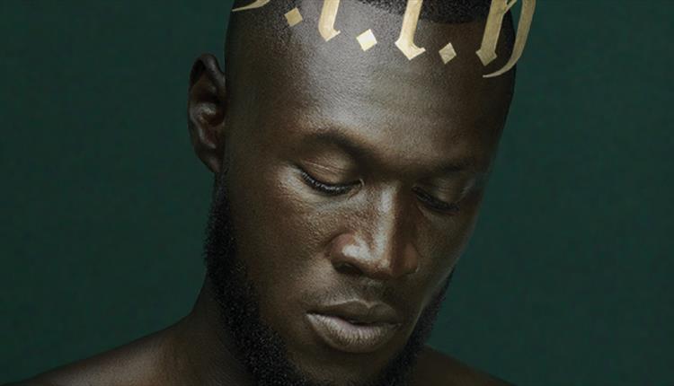 A man looking down to the floor with a 
 dark green backdrop behind him.