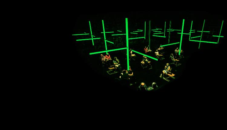 A black setting, participants sit underneath neon green strip lighting.