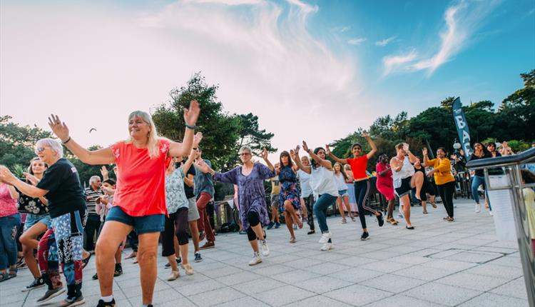 Crowd of people dancing in a sunny, outdoor location.