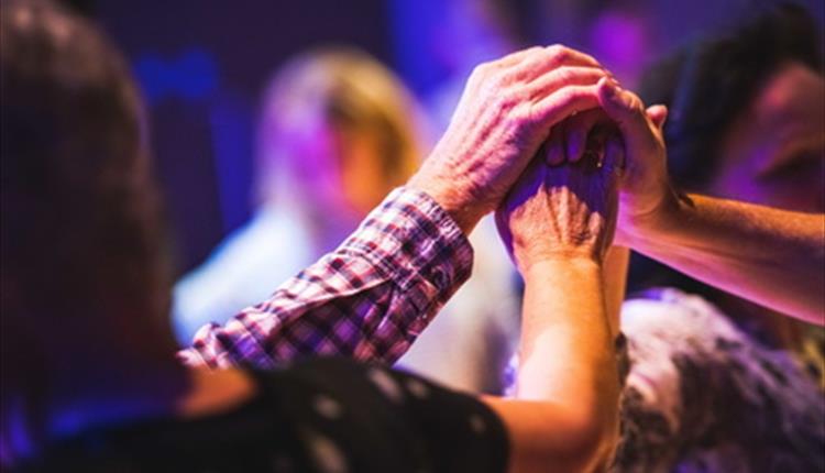 A group close up with clasped hands dancing Christmas Ceilidh