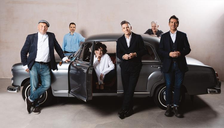 the current band line up standing in or by a classic car