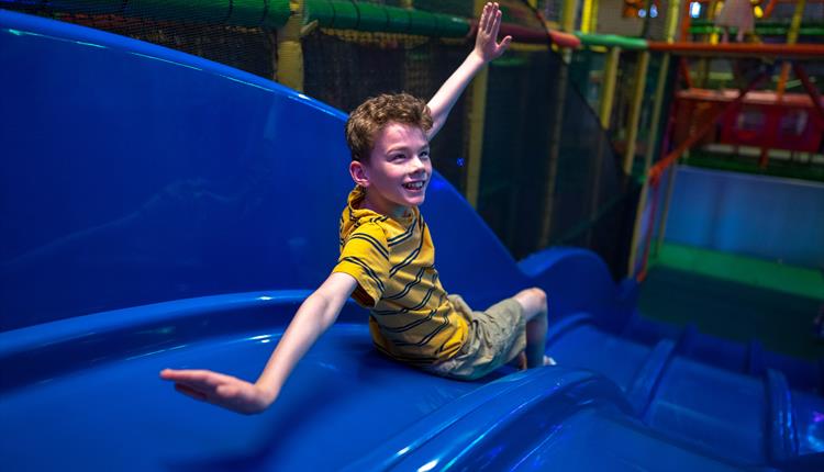 boy in a yellow shirt going down a blue slide