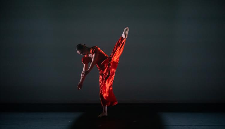 A dancer in red silk with leg extended above shoulder