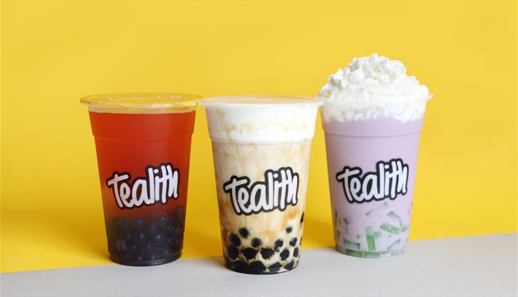 A shot of three bubble teas on a yellow background; one red, one creamy and one purple with foam.