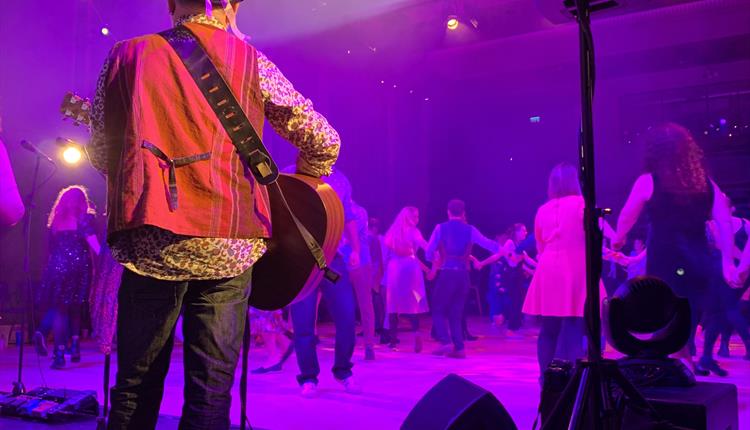 Back of man in hat playing banjo to a dancing audience