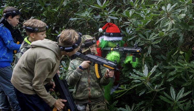 Grinch in a Christmas hat with a paintball gun hiding in the trees with four boys