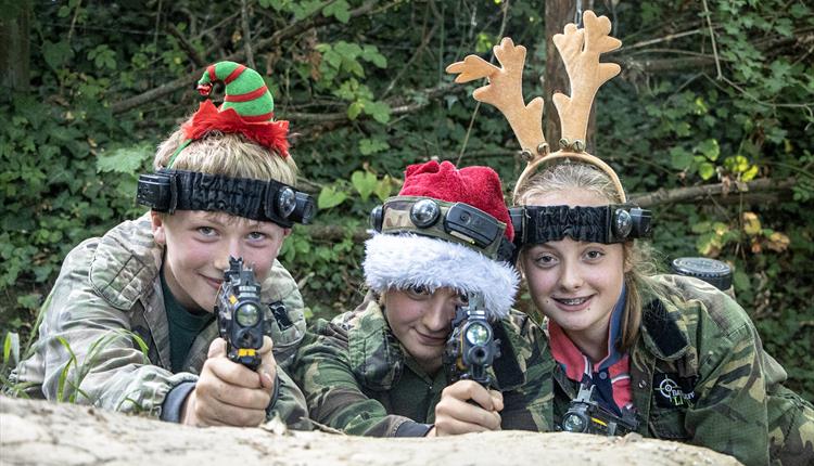 Children wearing camouflage clothing with Christmas hairbands on and holding toy guns.