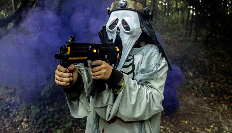 A person in a scream mash with a gun and purple smoke behind them