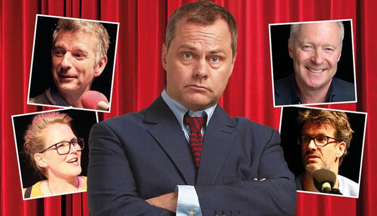 Comedian Jack Dee looking at camera with photos of other comedians around him