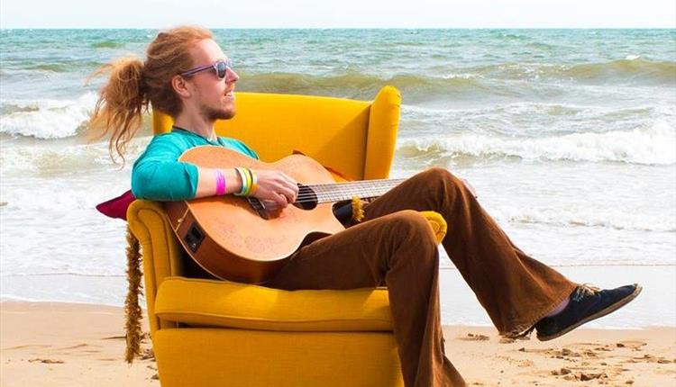 Picture of Jonny Phillips on the beach playing a guitar