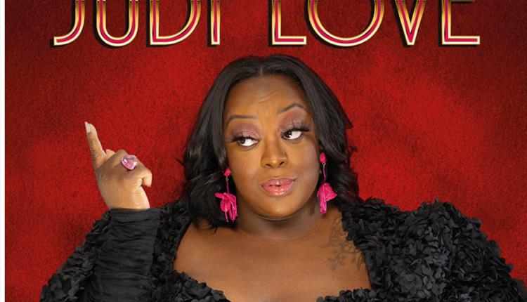 Comedienne Judi Love in a black dress against a red background