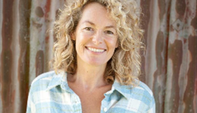 A lady with a blue and white checked shirt on, stood with her hands in her pockets.