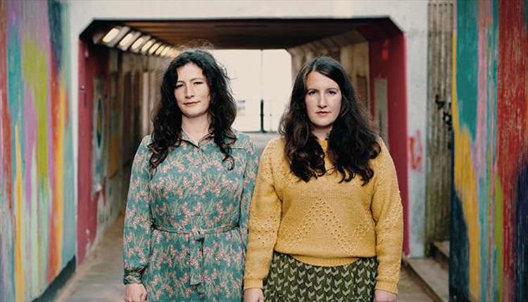 Two woman stood in a colourful underpass.