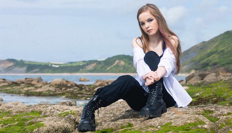 Young girl sitting on a rocky hillock overlooking a bay.