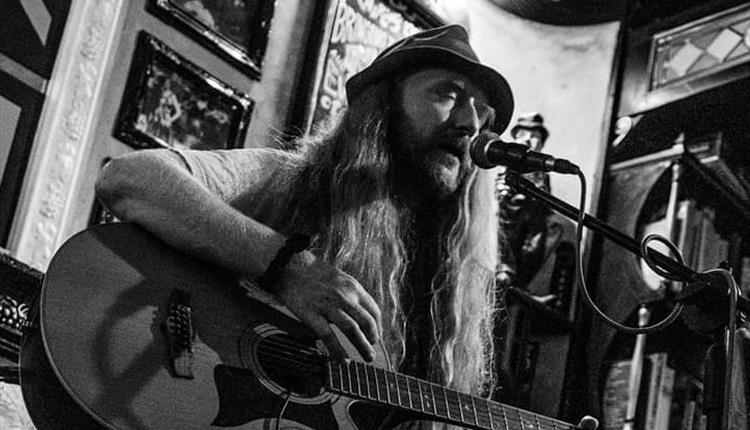 Black and white image of long haired man playing guitar singing into a microphone