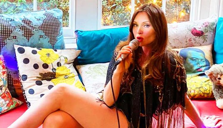 A woman siting with a microphone, on a sofa with glittery cushions