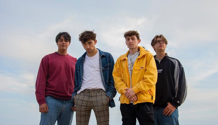 Four young men in casual wear facing front with only the sky as a background