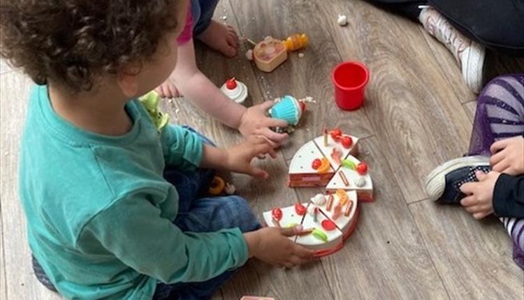 Several children sit together playing with a set of wooden toy food items.