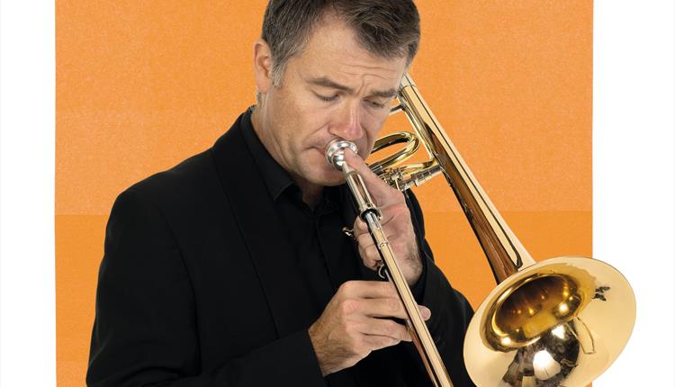 A BSO musician is playing the trumpet in front of an orange graphic.