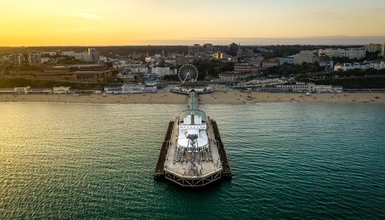 Drone shot of Bournemouth Pier and the surrounding beach area as the sun sets in the distance