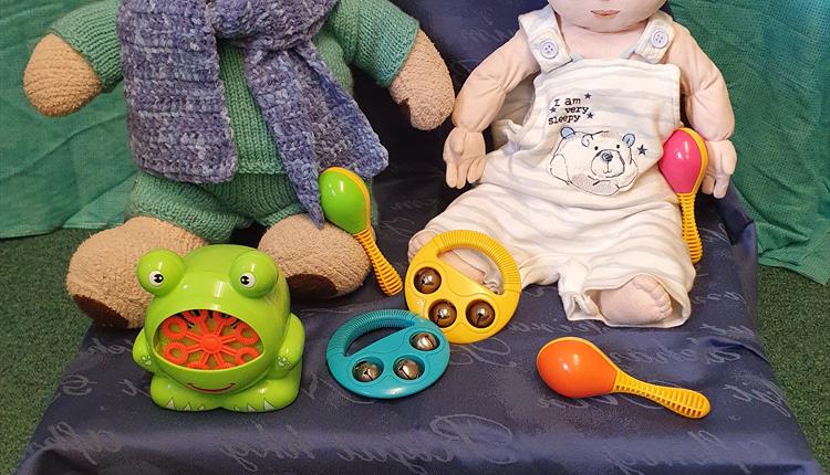 A toy baby and a teddy surrounded by musical instruments