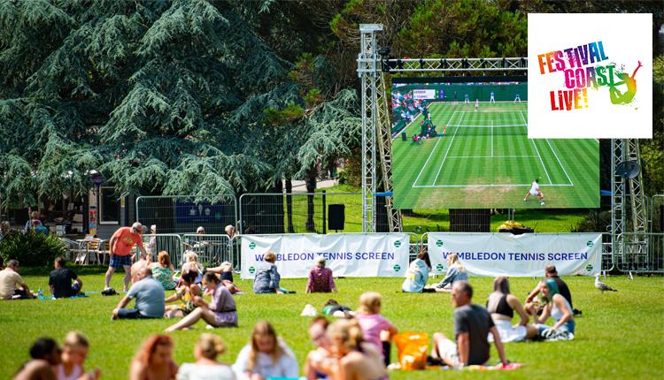 Large screen in the gardens with people sitting on the grass