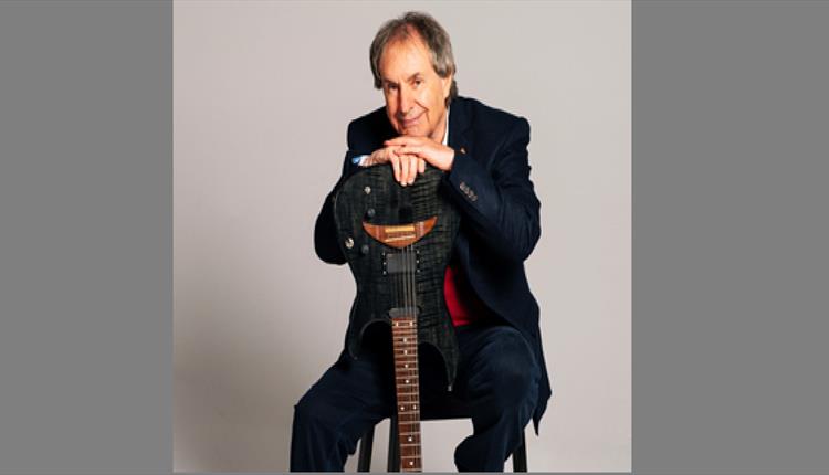 Musician Chris De Burgh sat facing camera with hands resting on an upsidedown guitar