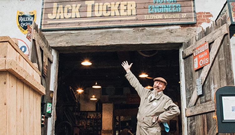 Man dressed in overals with moustache pointing to sign