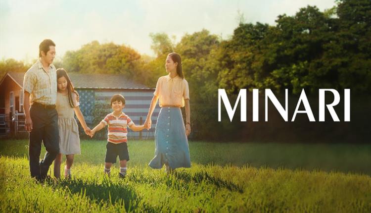 Two parents and two young children hold hands as they walk through a sun soaked field.