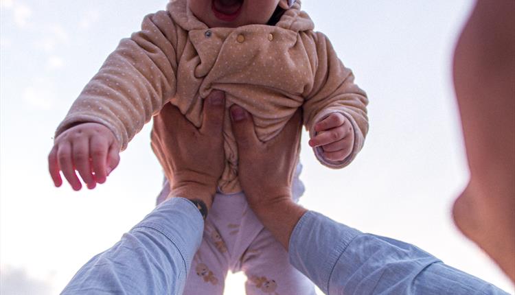 A smiling baby being hoisted lovingly in the air.