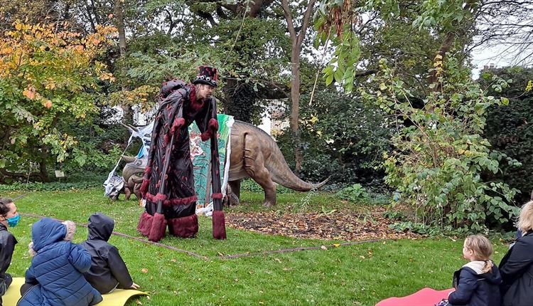 A man dressed up in the Red House Museum Garden with children sat watching a performance.