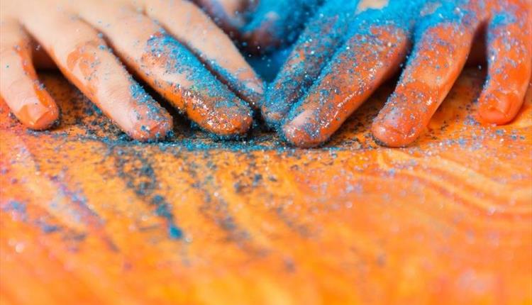 A child's hands covered in blue glitter on a wooden table.