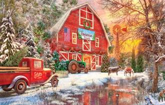 A red barn with a green tractor outside with snow on the ground and two cows in the background