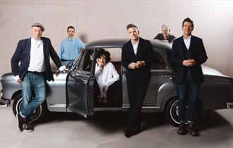 the current band line up standing in or by a classic car