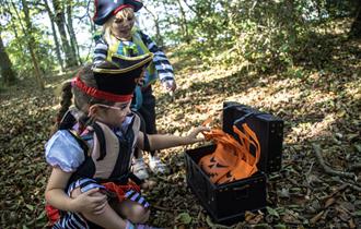 Two young children in pirate fancy dress opening a treasure chest