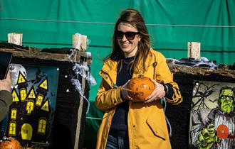 Lady holding a pumpkin in a yellow coat smiling at the camera