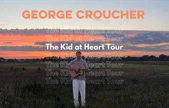 George Croucher in a field at sunset with a guitar in his hand