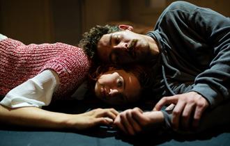 A photo of Sunnyside by Northern Rascals. A close up shot of two people, a man and a woman, lying down. The woman has her head on the floor and the ma