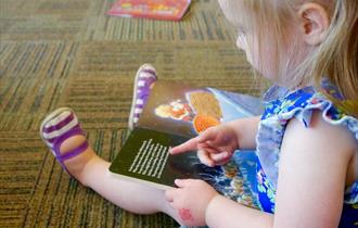 A young girl sitting on the floor reading a book